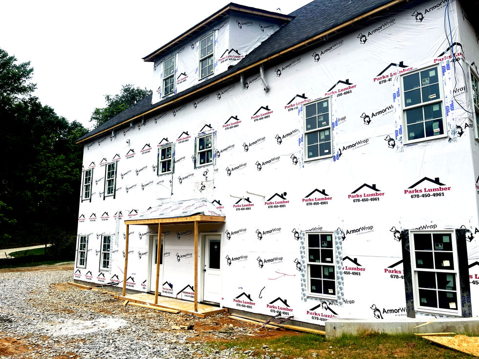 Construction progress photo of the rear elevation of a modern duplex in Dahlonega, Georgia, showing installed windows, roofing, weather-resistant building wrap, rear entry canopies, and exterior envelope work prior to siding installation. 
