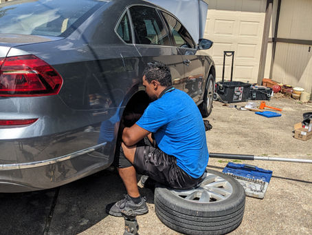View of mechanic performing brake repair services on a gray sedan.