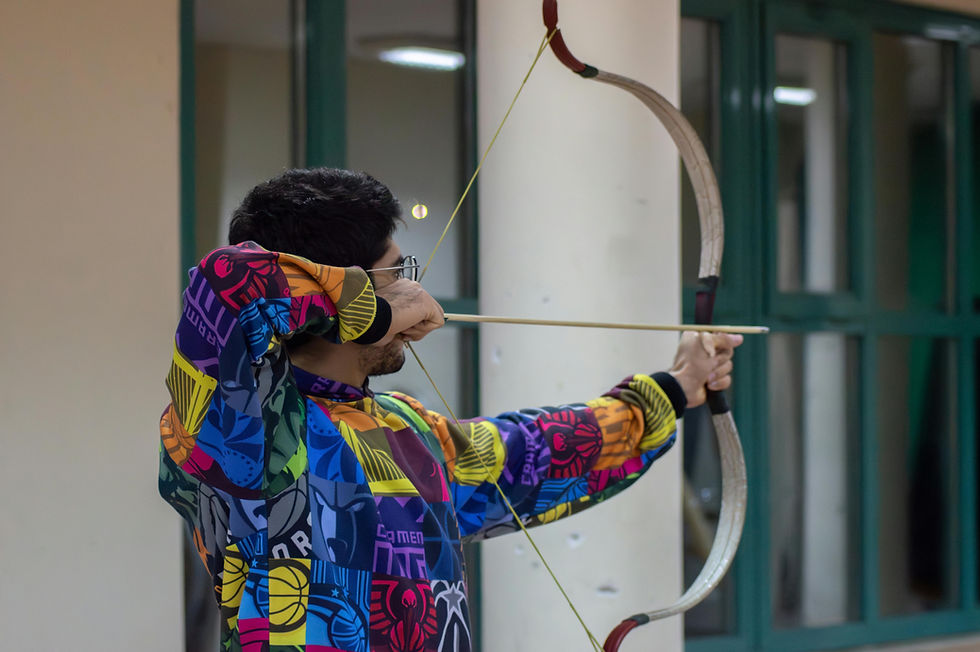 A photo of a young man aiming at a target with a bow and arrow.