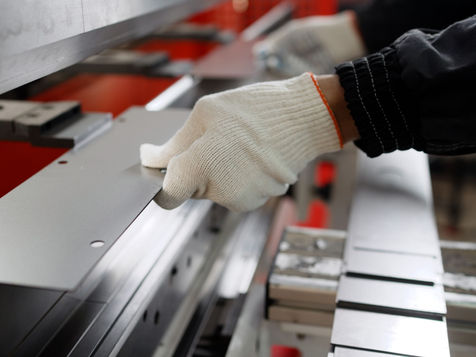 Operatore con guanti lavora una lamiera su macchina piegatrice