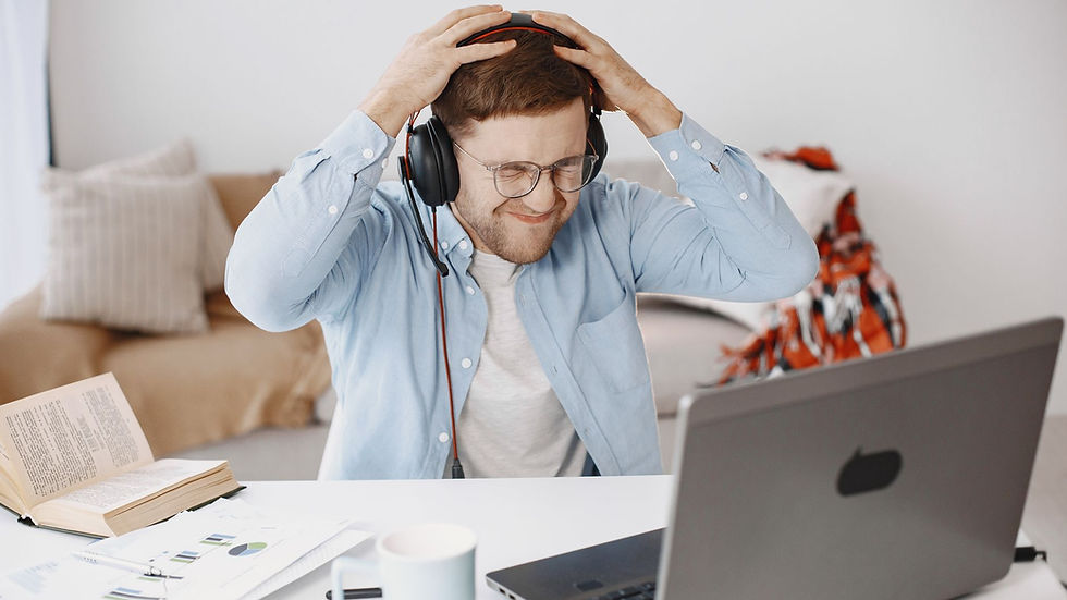 A frustrated man with headphones working at home office, laptop on desk.
