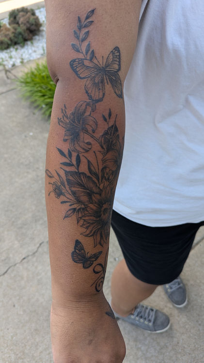 Black and white tattoo on a person's arm of flowers and butterflies
