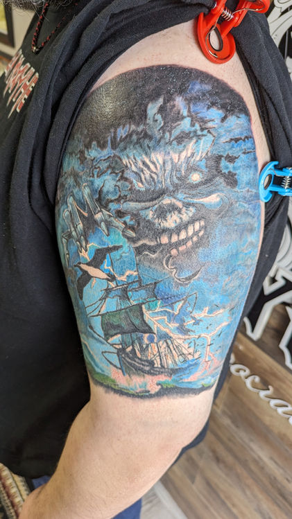A man's arm with a tattoo of a skull, a ship, and lightning