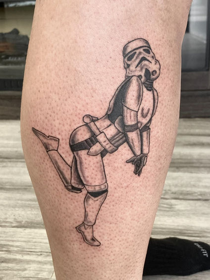 A black and white tattoo of a Stormtrooper on a person's leg