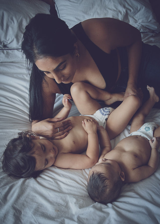 A mother with her two babies, just in nappies, lay cuddling on a bed. Th
