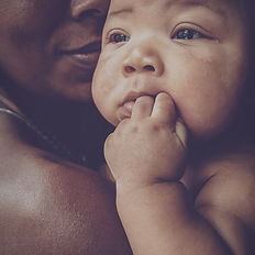 Black mother and her baby cuddling baby has fingers in his mouth
