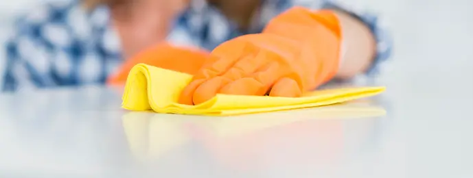 alt="Professional cleaning service in Marbella wiping a surface with a yellow microfiber cloth and orange gloves."