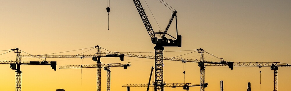 Several large cranes against a rosy skyline