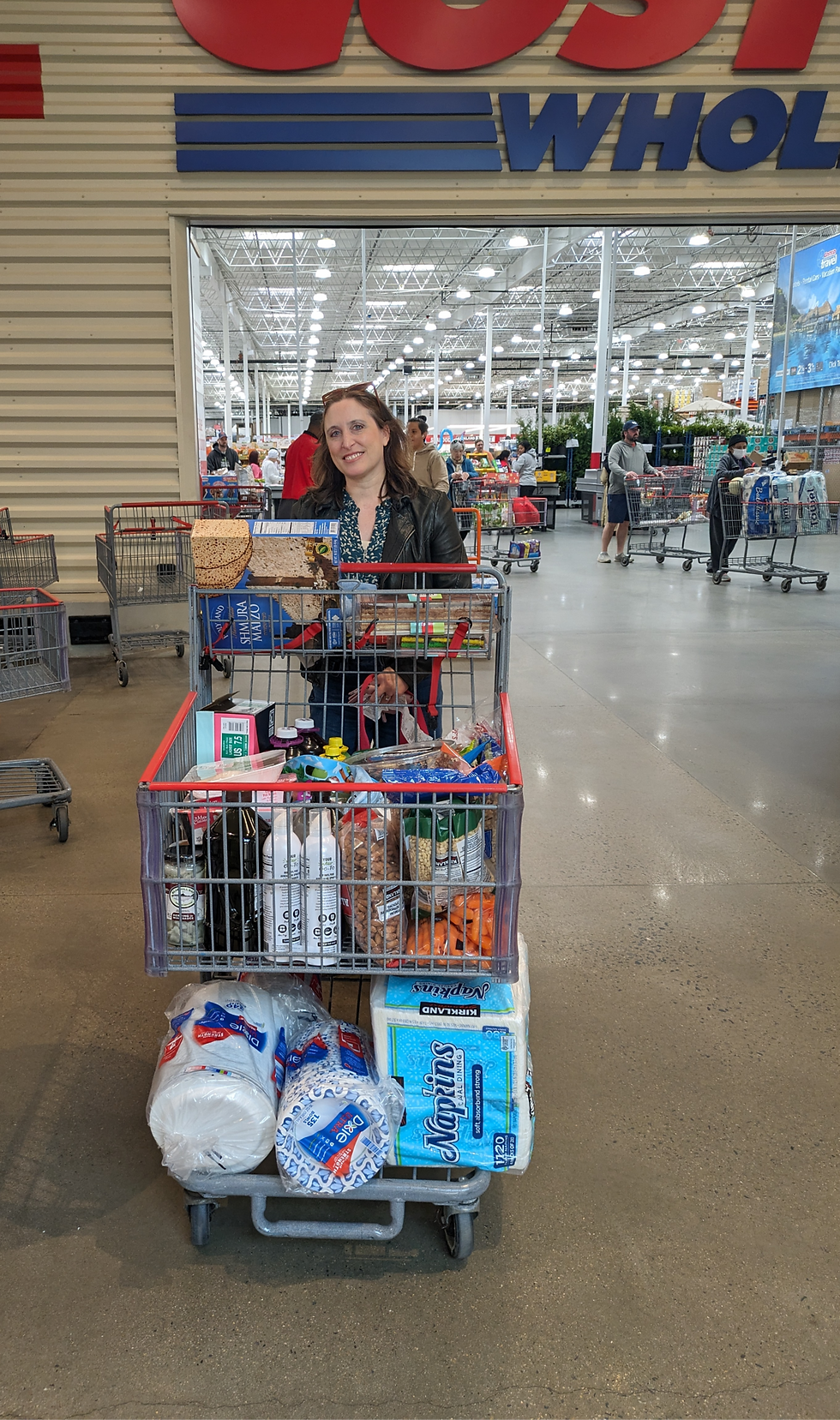 Woman smiling and standing behind a full shopping cart in front of Costco