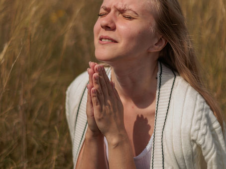 A woman kneeling in prayer in a field, her face reflects earnest prayer