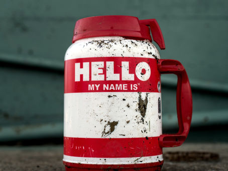 A red and white, dirty, thermal jug with the name tag design on it that says "Hello my name is" left blank.
