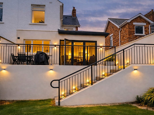 Rear extension with large sliding doors and terrace lighting connecting home to gardens overlooking Greenville Park in Belfast by GT Building Design.