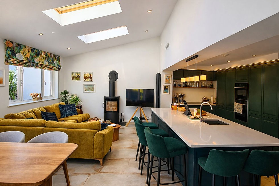 Open‑plan kitchen and living area in Donaghadee featuring dark green cabinetry, skylights, and a cosy family space designed by GT Building Design.