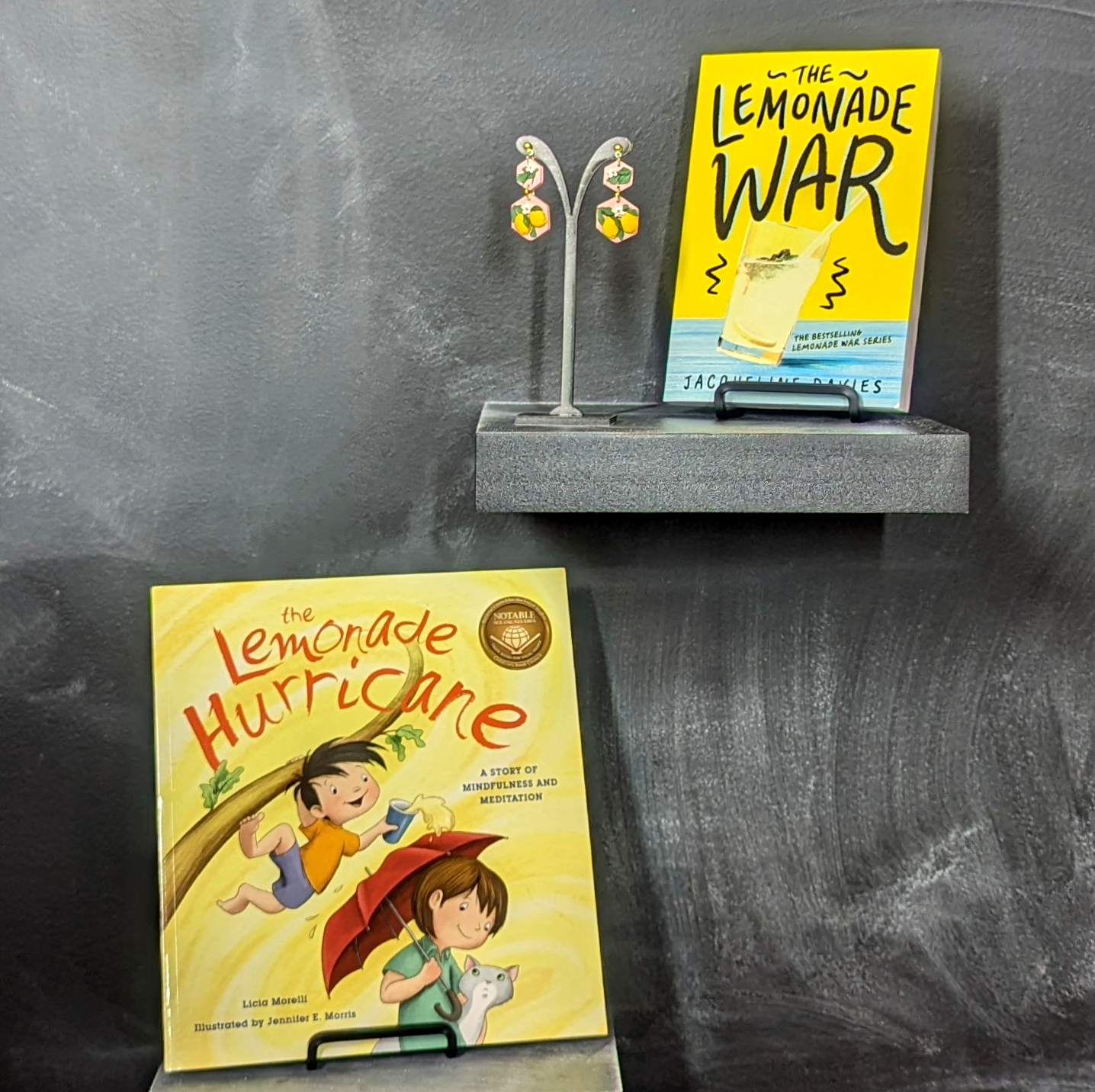 Picture of clay polymer statement earrings with lemons, the chapter book The Lemonade War, and the picture book The Lemonade Hurricane.