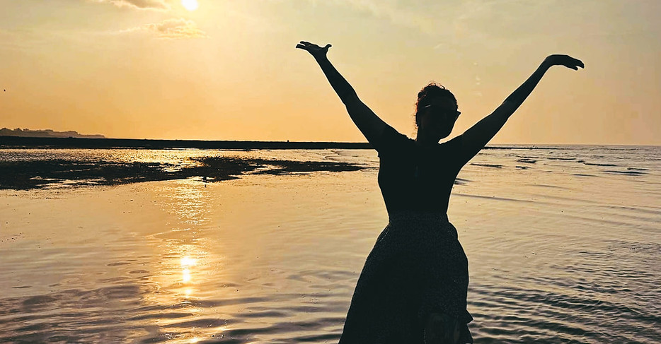 Girl with her arms in the air on the beach with a sunset in the background