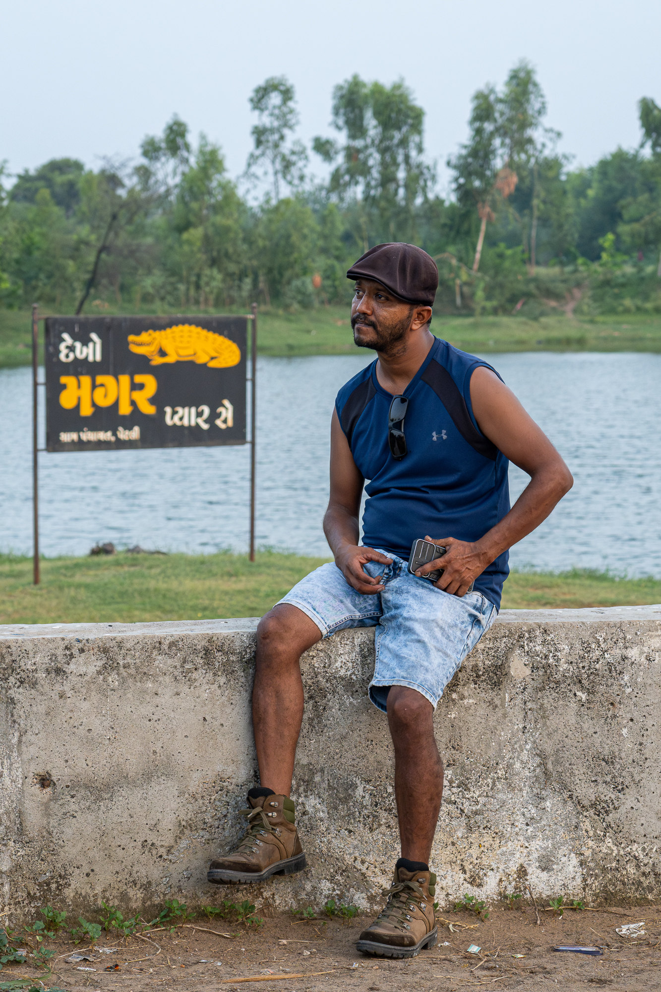 Vishal sits on a low wall by the lake, the Dekho Magar Pyaar Se sign behind him