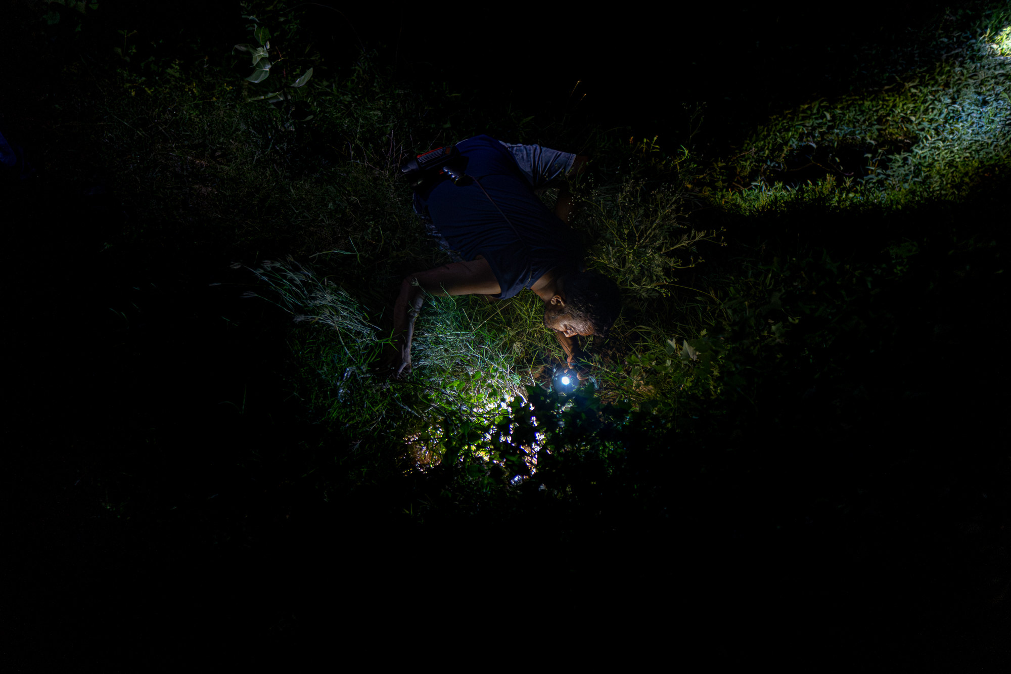 Vishal crouches in long grass at night, shining a torch into a den