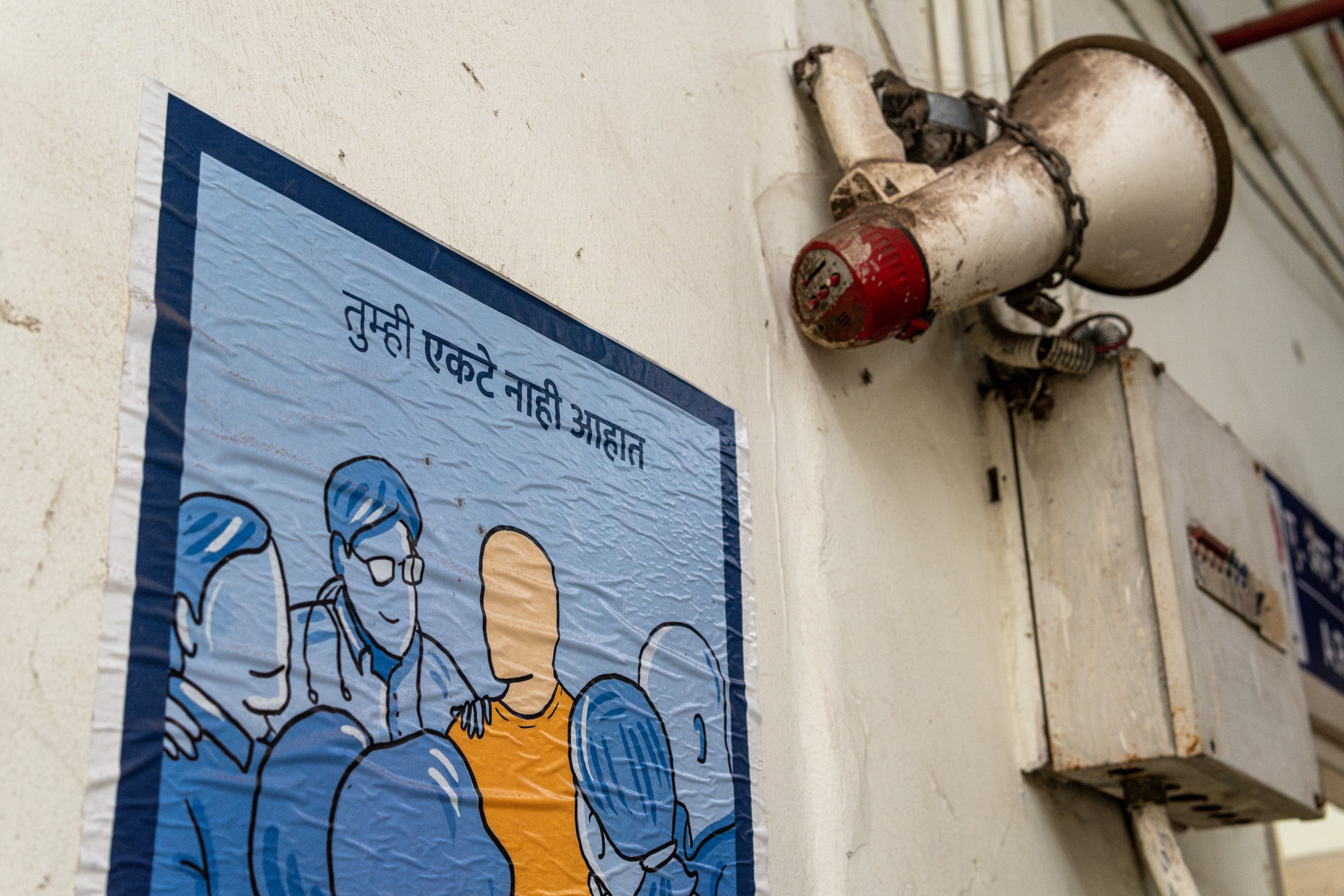 A Marathi poster showing a figure surrounded by supportive people, mounted beside an old loudspeaker