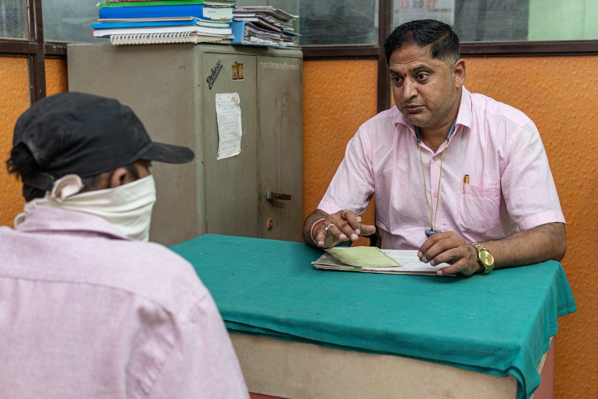 A counsellor in a pink shirt speaks with a client whose face is covered with a cloth