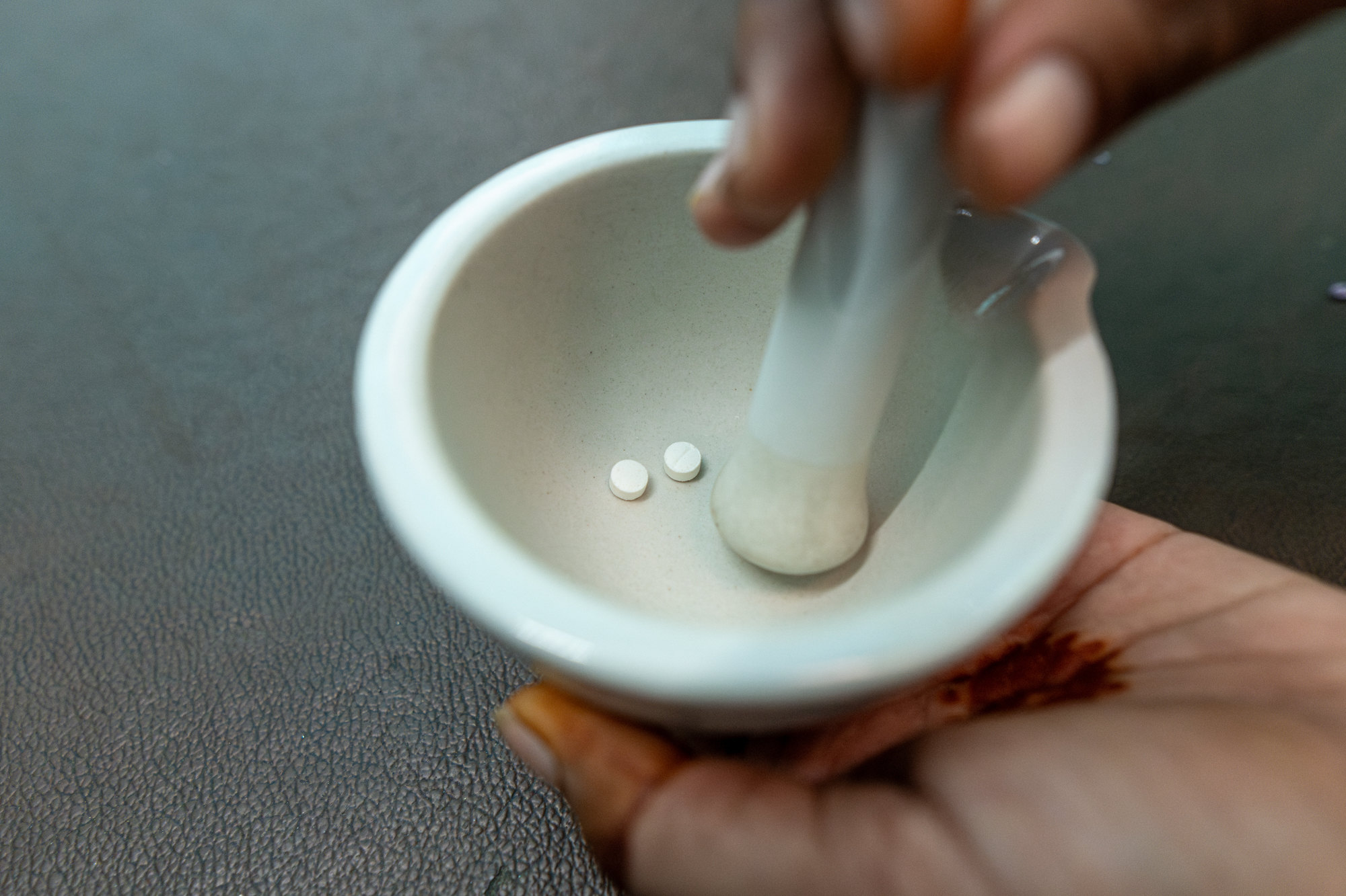 Two white OST tablets in a mortar as a hand holds the pestle
