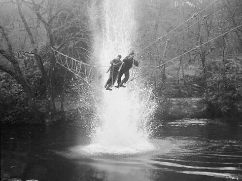 Commandos_cross_a_river_on_a_toggle_bridge_under_simulated_artillery_fire_at_the_Commando_