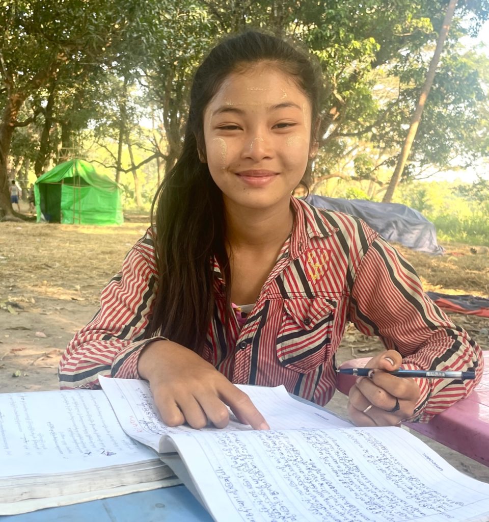 Young Karen girl continues studying in hiding place as shells land nearby.