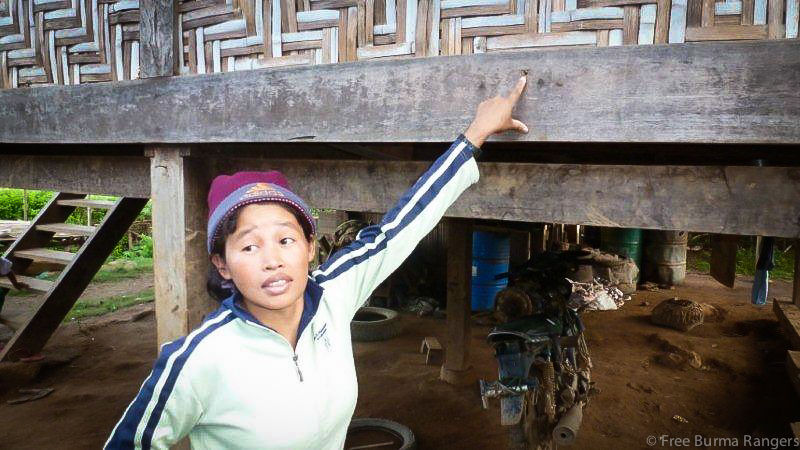 Ji Tawng stands outside her home and points to bullet holes from Burma Army attacks in December 2011