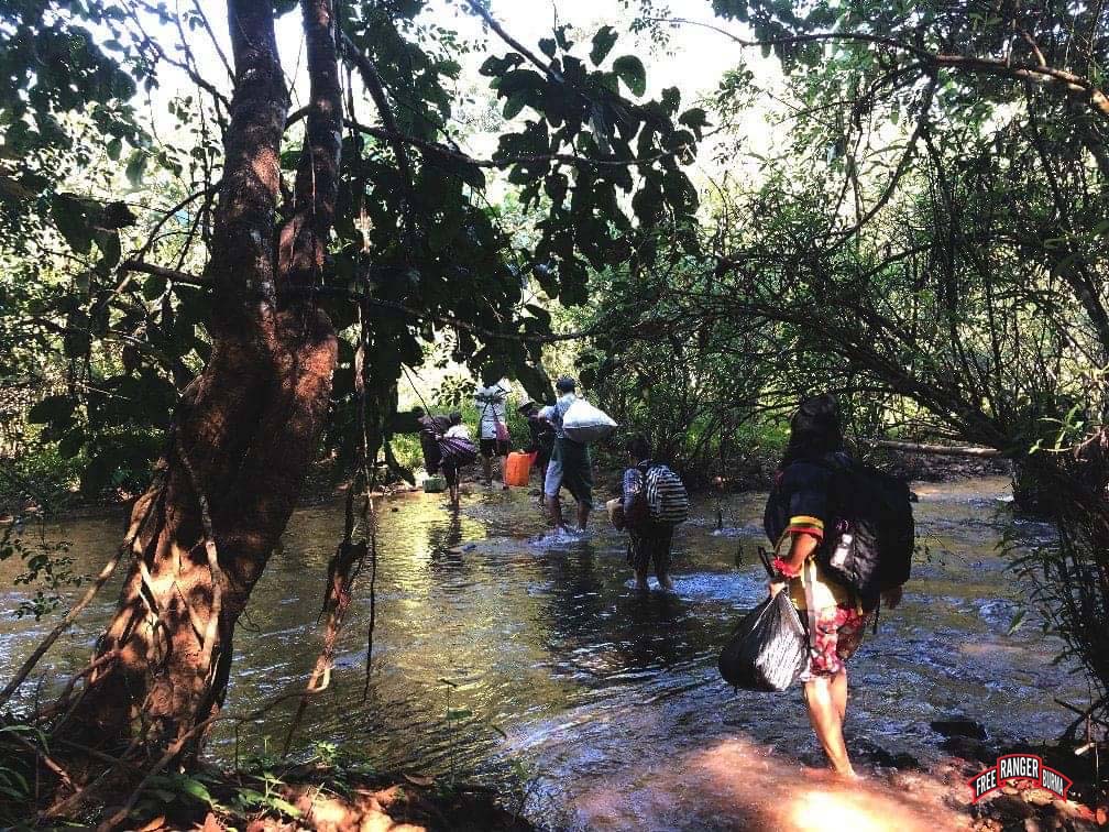 IDPs cross a stream while carrying what they can from their homes
