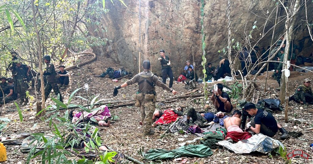 Medics triage casualties at mobile clinic under a big rock.