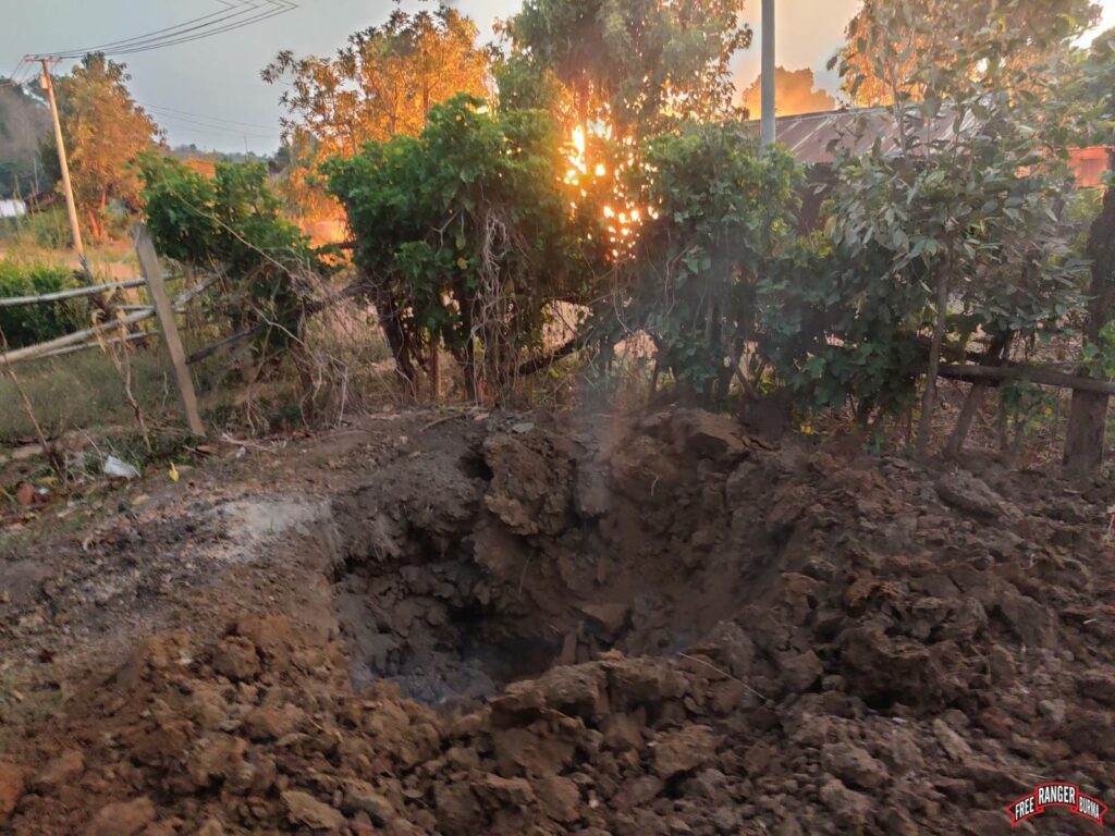 A bomb crater next to a house burning after airstrikes in South SaLone Village.