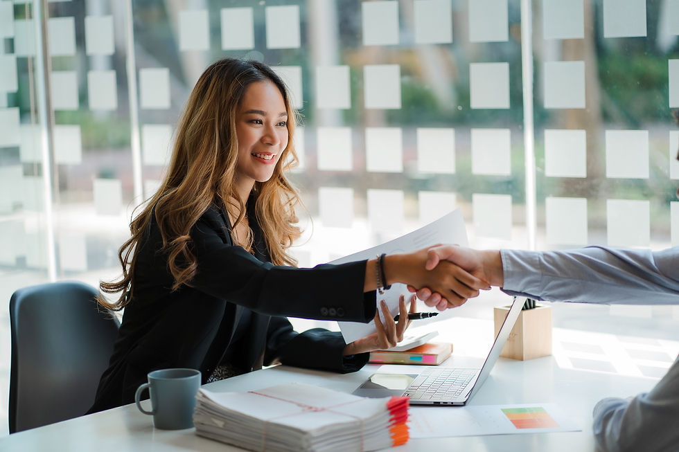 Woman shaking hands with a colleague, paperwork and laptop on desk setting.