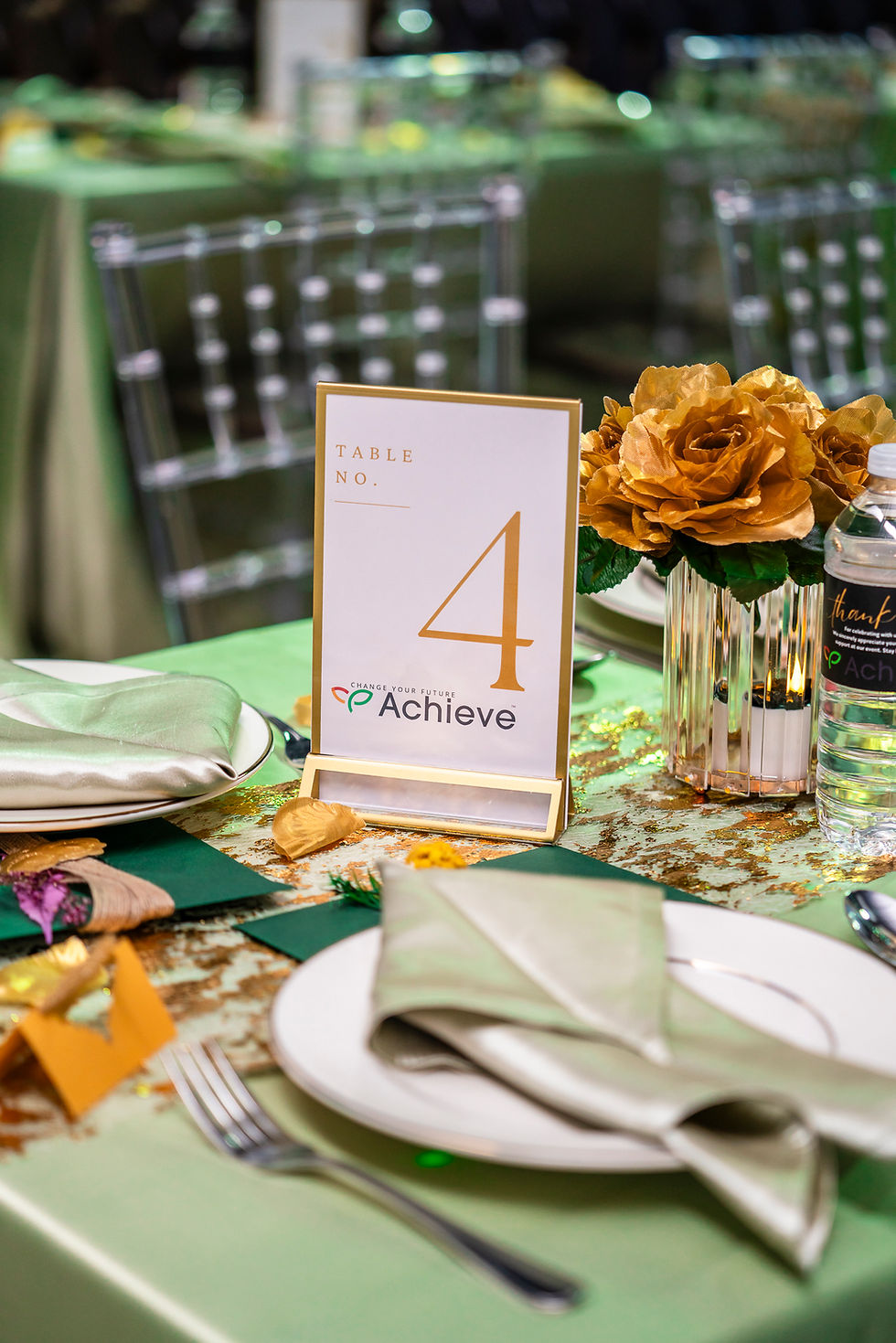 Table setting with number four, Achieve logo, and gold floral arrangements.
