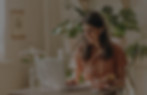Woman using laptop smiling while working with plants and coffee in background.