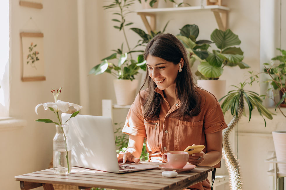 Woman working on laptop with a coffee, surrounded by plants, smiling and happy.