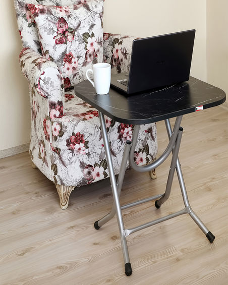 Halley Serisi 50x60 cm masa tablası, üzerine dizüstü bilgisayar yerleştirilmiş şekilde bir sandalyenin önünde konumlandırılmış. Bu kompakt masa, dizüstü bilgisayarlar için mükemmel bir çalışma alanı sunarak ev ofisleri, çalışma alanları veya yaşam alanlarında gündelik kullanım için ideal bir seçenek oluşturur.