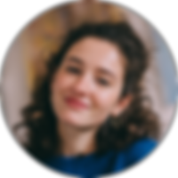 Indoor portrait of a young woman with curly hair, smiling warmly.