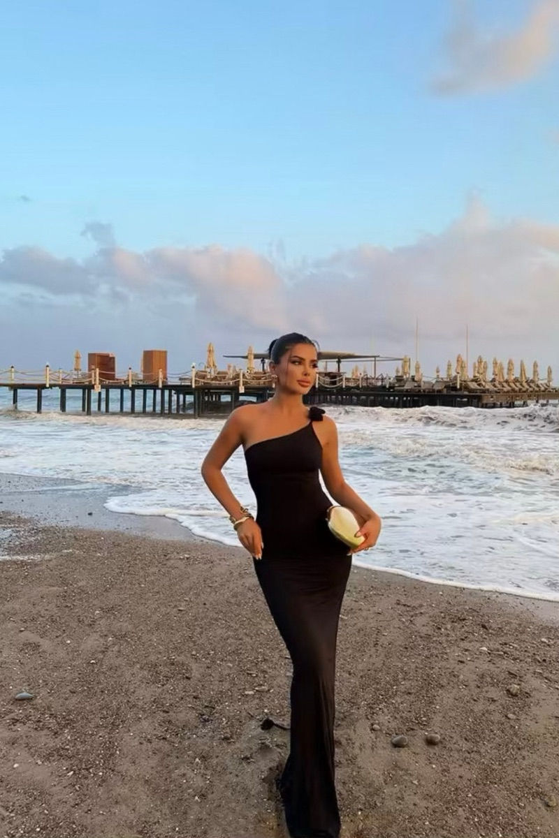 Miniature : femme portant une robe longue noire moulante asymétrique avec une bretelle ornementée de détails floraux