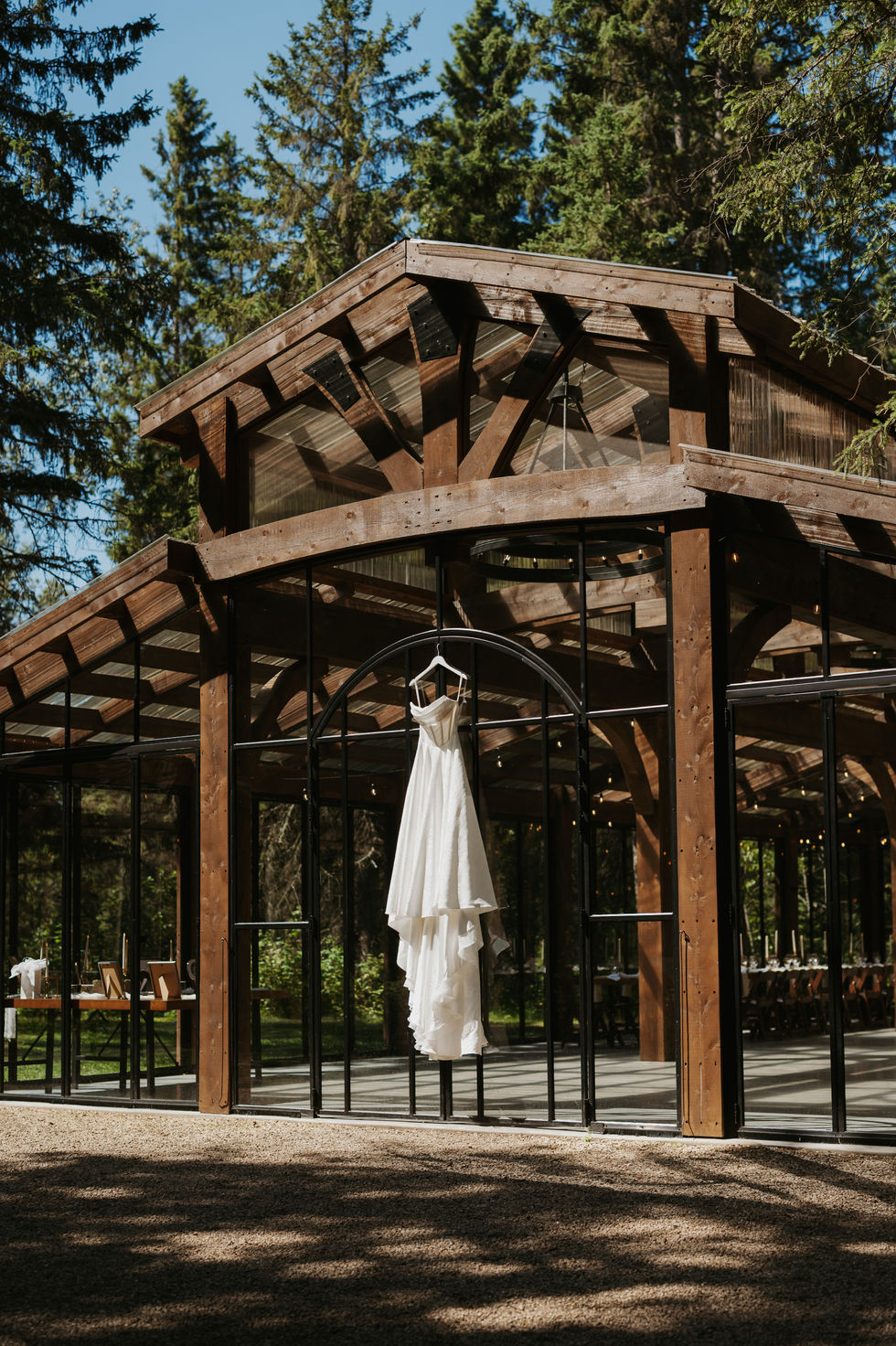 White wedding dress hanging outside the glass and timber reception venue at The Valley in Alberta.