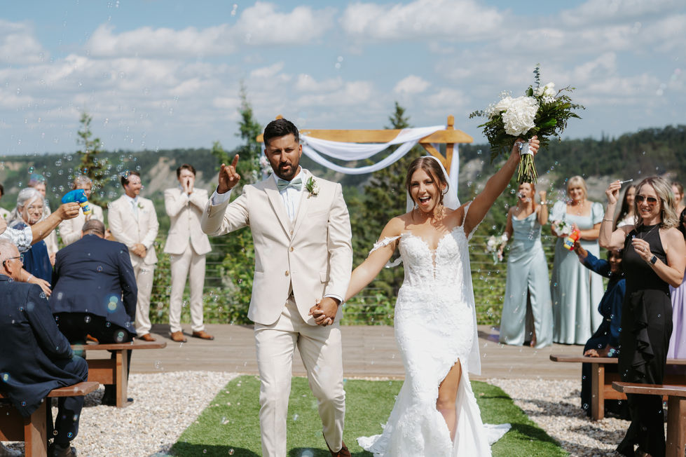Newlywed bride and groom walking hand in hand through bubbles after their outdoor ceremony at River’s Edge Devon.
