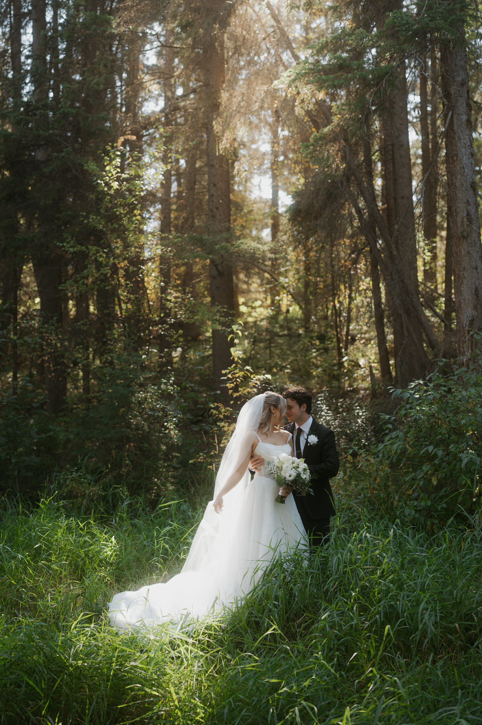 Bride and groom embracing in a sunlit forest during wedding portraits at The Valley near Edmonton.