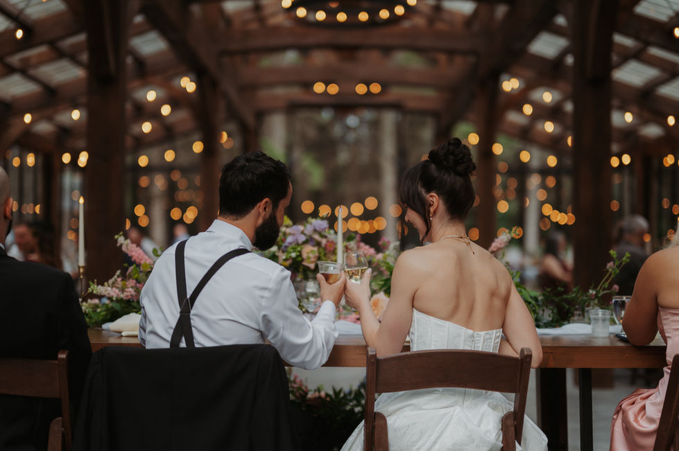 Bride and groom seated at a long reception table with colourful flowers and candlelight.