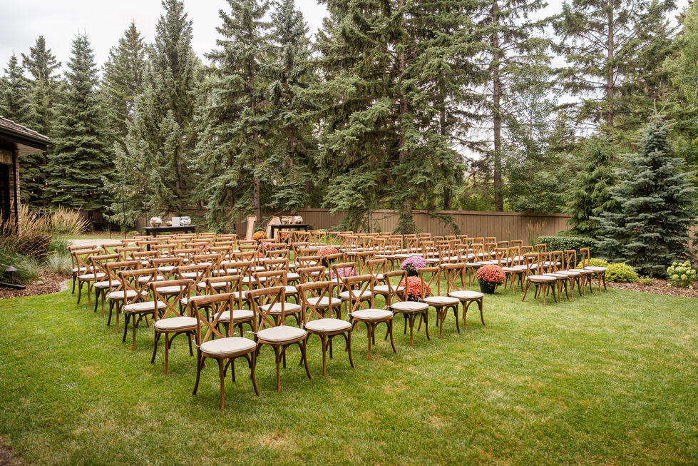 Edmonton backyard wedding ceremony setup with wooden chairs surrounded by mature trees and greenery.