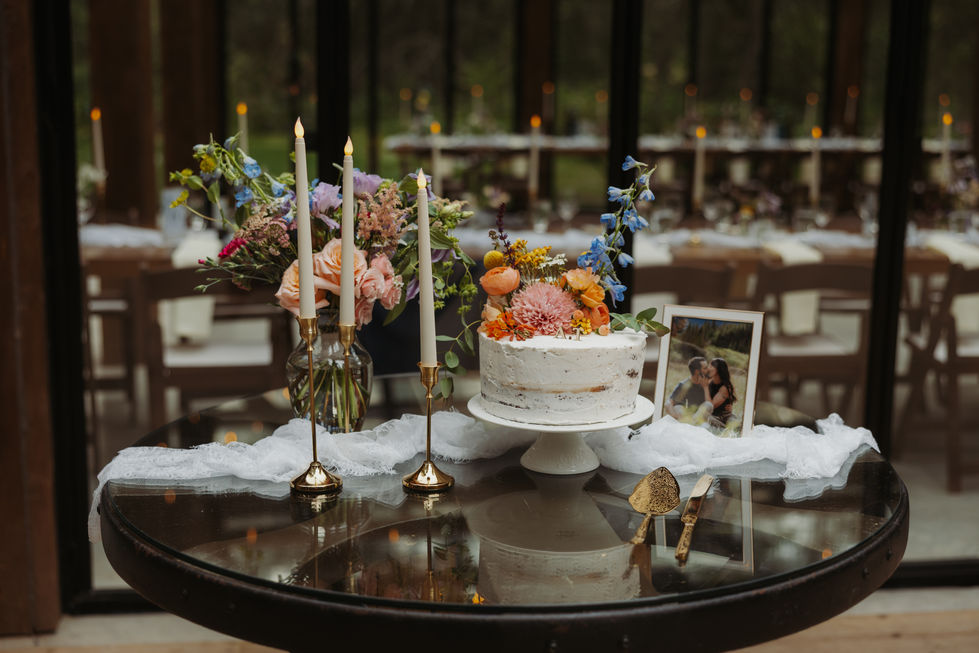 White wedding cake decorated with colourful flowers inside The Valley wedding reception.