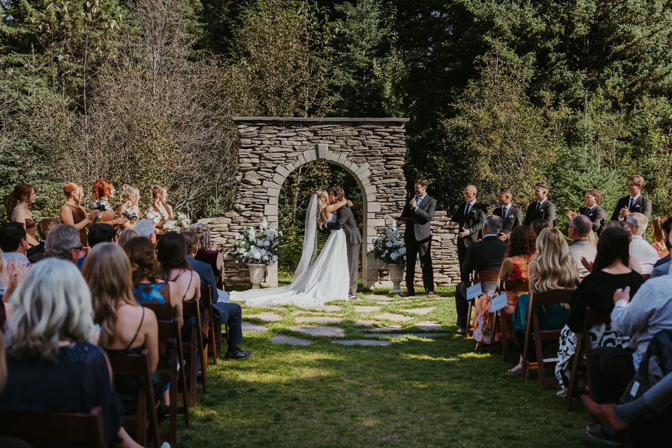 Outdoor woodland wedding ceremony with bride and groom beneath the stone arch at The Valley in Alberta.