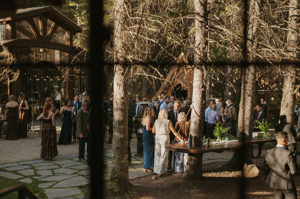 Wedding guests gathered for cocktail hour beneath the trees outside The Valley wedding venue.