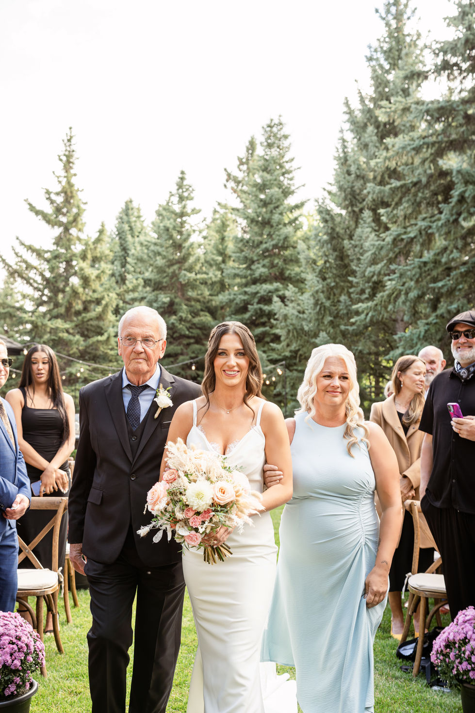 Bride walking down the aisle with her parents at an intimate backyard wedding ceremony.