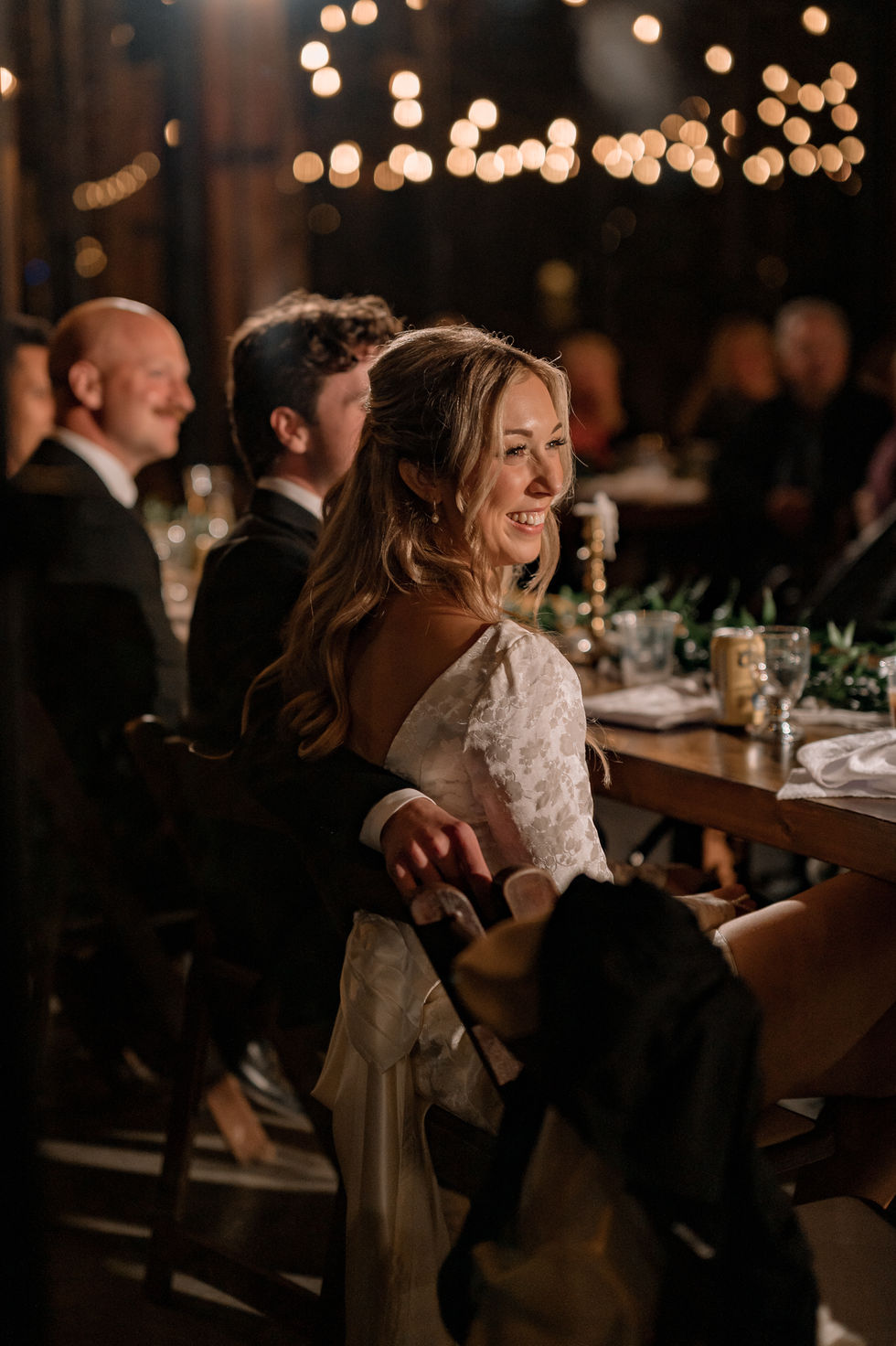 Bride seated at her evening wedding reception beneath warm string lights at The Valley in Alberta.