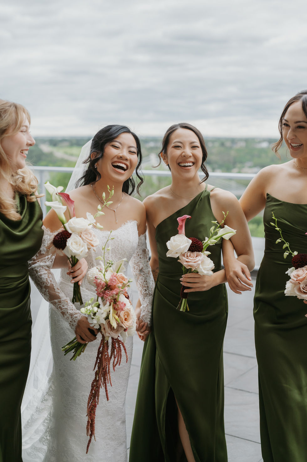 Bride laughing with bridesmaids in olive green dresses during pre-ceremony wedding portraits in Edmonton.