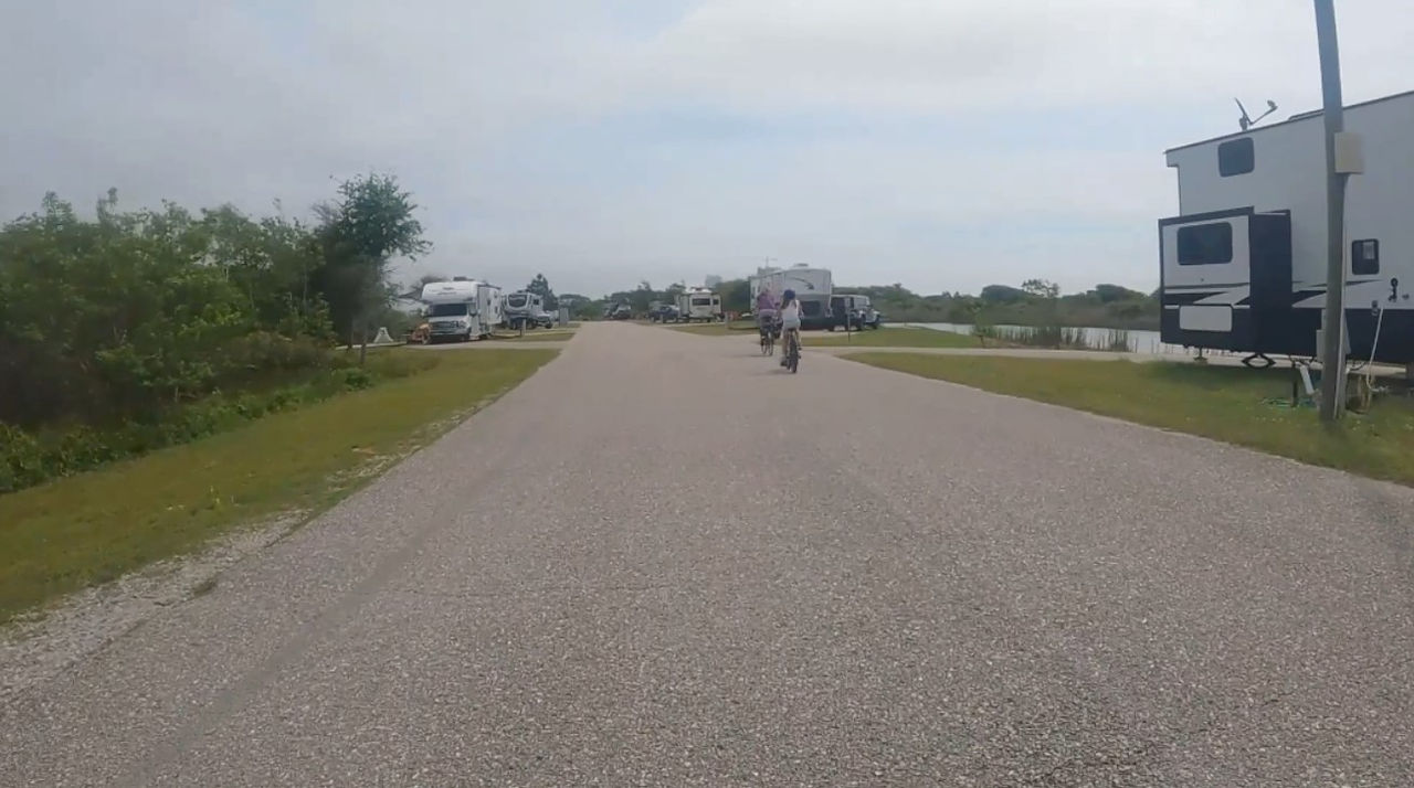 kids riding bicycles through gulf state park campground with pull through campsites on either side of the road and a waterway in the distance on the right.