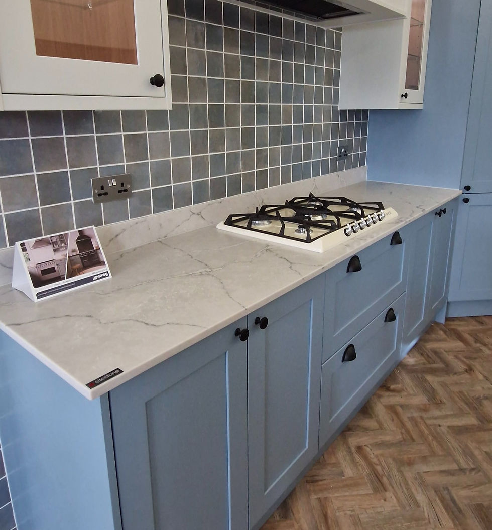 Coastal mist light blue kitchen with Matt black handles, warm herringbone flooring, tiled backsplash and grey quartz worktop.